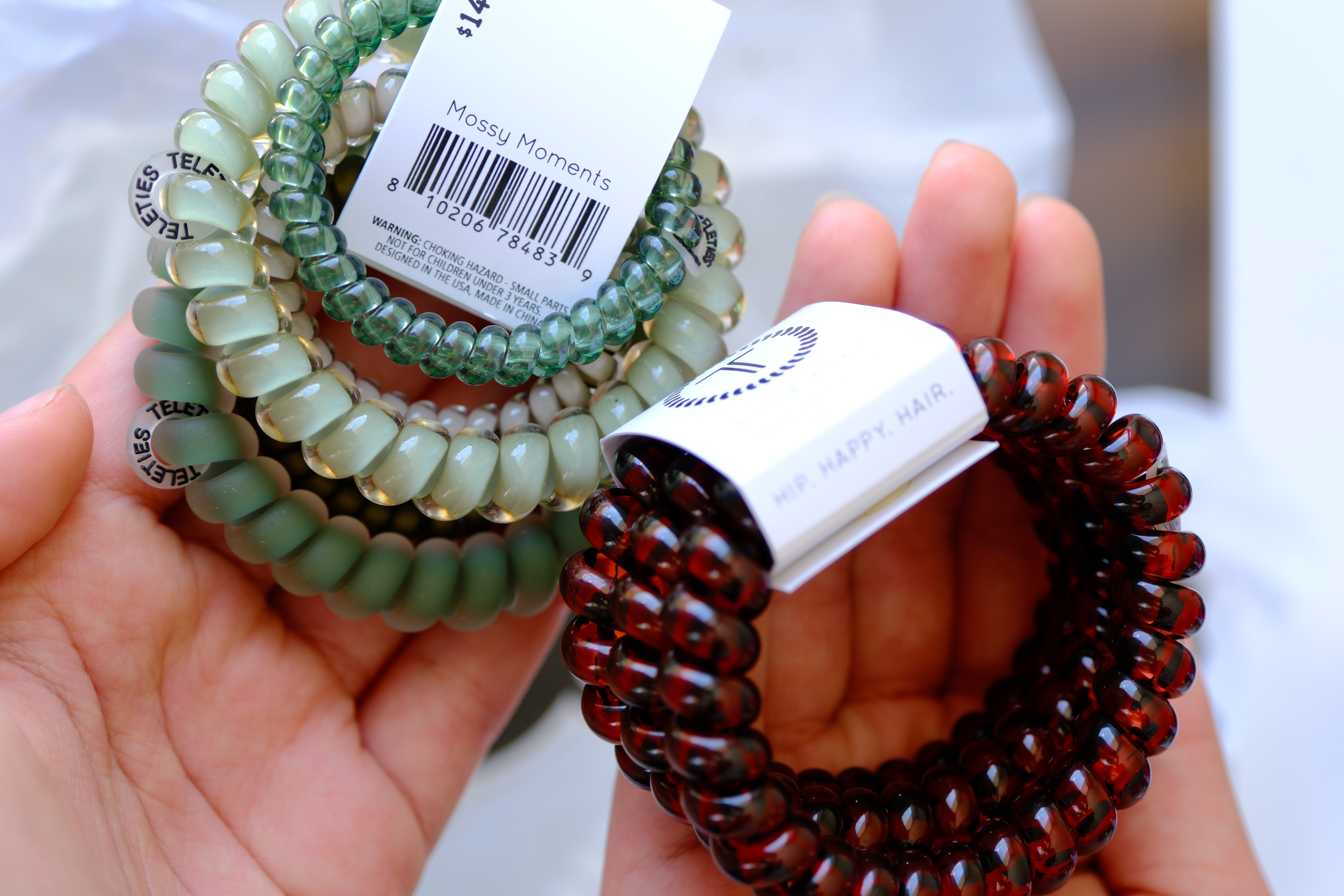 Close up of TELETIES Mossy Moments mix pack and Tortoise large spiral hair ties held in Amanda's hands