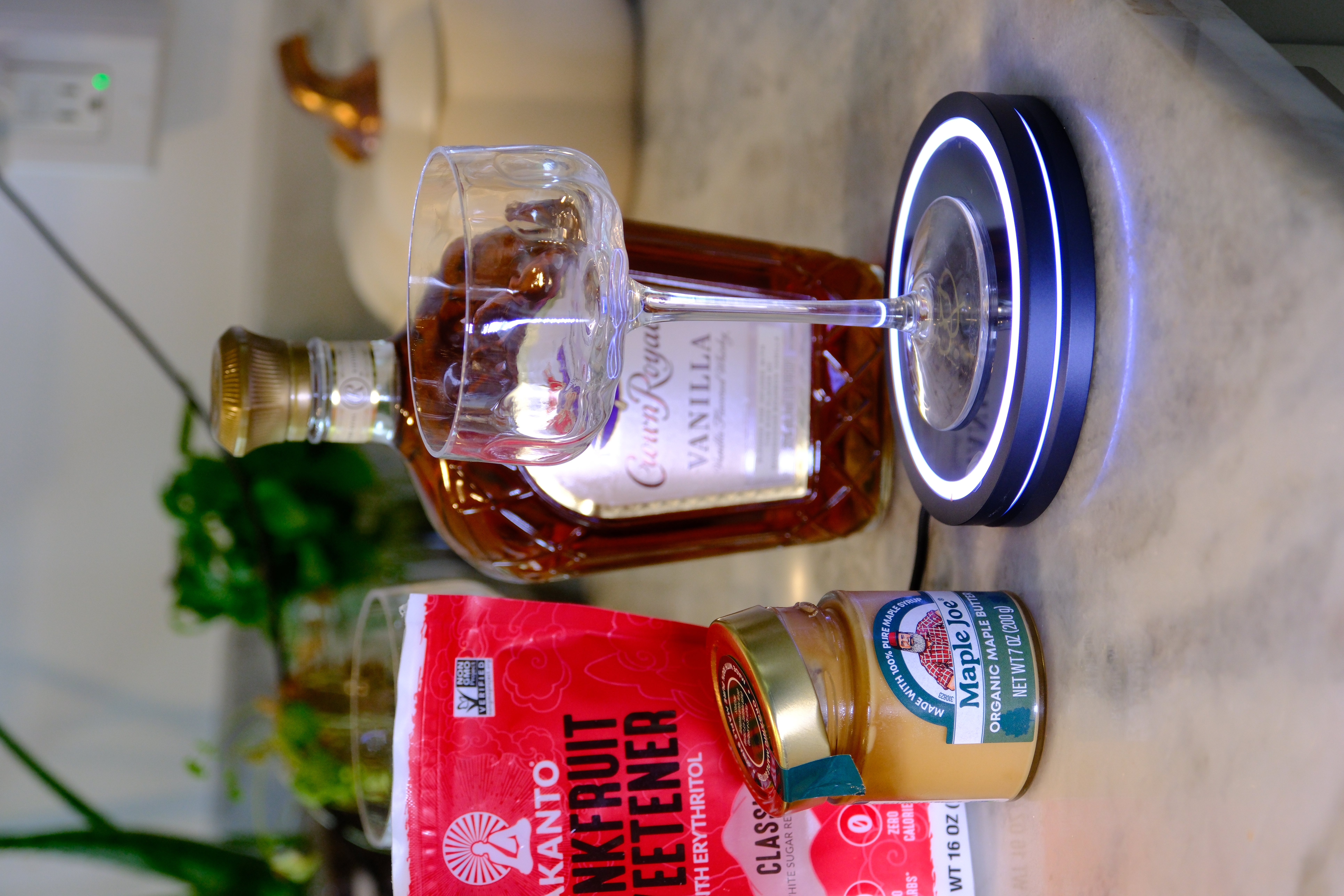 Barsys Smart Coaster 2.0 smart cocktail coaster lit up under an empty coupe glass beside Crown Royal Vanilla and maple syrup, gifted to lifestyle influencers Alex and Amanda of Salty Vagabonds. Barsys promo code SALTYVAGABONDS20 for 20% off at barsys.com